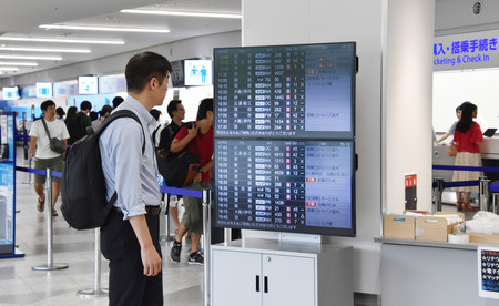 福岡空港で運航予定を知らせるモニターを見る利用客=14日午後、福岡市博多区