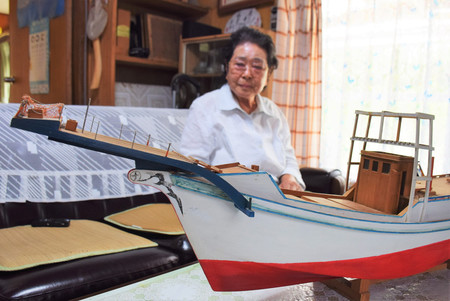夫が所有したというカツオなどを捕る漁船「突き棒船」の模型と、長浜智恵子さん=4月23日、沖縄県与那国町