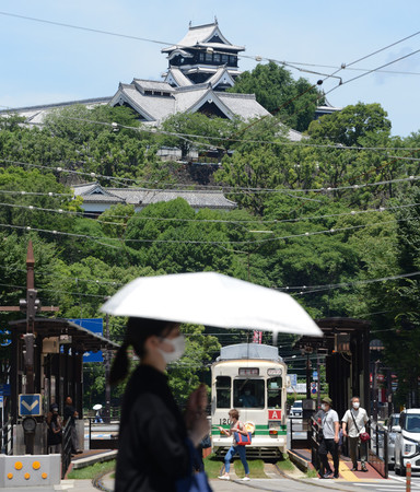 厳しい日差しの中、日傘を差して歩く人(後方は熊本城)。気象庁は28日、九州北部と四国、中国、近畿、北陸の各地方が梅雨明けしたとみられると発表した=同日午前、熊本市中央区