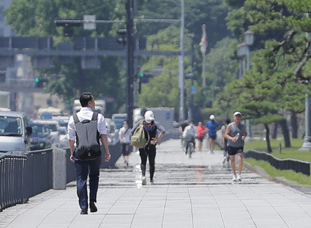 強い日差しの中、皇居沿いの道を行き交う人たち=29日午前、東京都千代田区