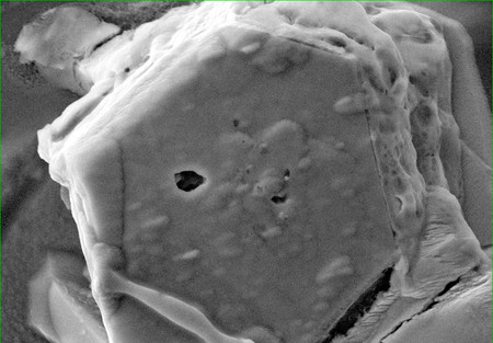 小惑星「りゅうぐう」の試料に含まれる硫化鉄結晶(六角形)。内部の穴(中央)から水が見つかった(NASA/JSC・東北大提供)