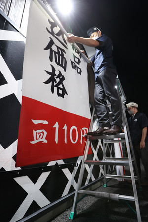 値上げ前の店頭タペストリーを取り外す回転ずしチェーン「くら寿司」社員=30日夜、東京都足立区のくら寿司足立栗原店