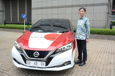 日の丸と赤白2色のインドネシア国旗をあしらった電気自動車(EV)の横に立つ田村政美次席公使=9月29日、ジャカルタ