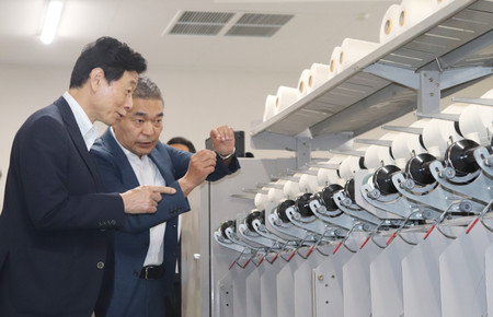福島県双葉町の撚糸工場を訪問し、説明を受ける西村康稔経済産業相(左手前)=17日午後、同町