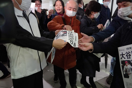 大谷翔平選手のMVP受賞を報じる新聞の号外を受け取る人たち=17日午前、札幌市