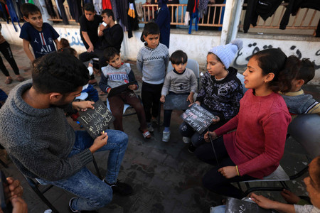 ２９日、パレスチナ自治区ガザ南部ラファの避難所で、男性から英語を教わる子供ら（ＡＦＰ時事）