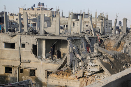 ６日、パレスチナ自治区ガザ南部ハンユニスで、イスラエル軍の攻撃を受けた建物を確認する住民（ロイター時事）