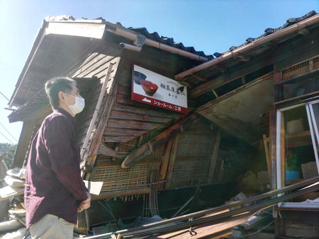 地震で倒壊した輪島屋善仁の倉庫と川越康さん＝３月２７日、石川県輪島市