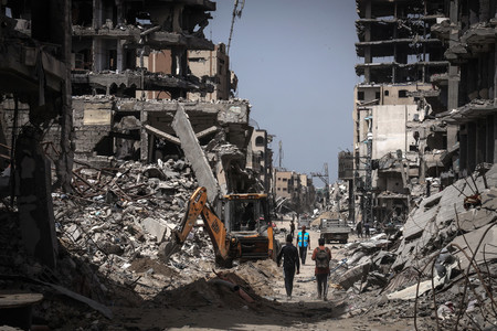 ２３日、パレスチナ自治区ガザ南部ハンユニスで、破壊された建物の間を歩く人々（ＡＦＰ時事）