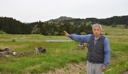 棚田が広がる集落について説明する井池光信さん＝４月２６日、石川県輪島市