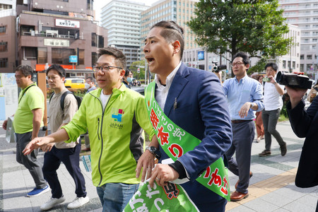 衆院東京１５区補選で、街頭演説を終えた他陣営の関係者を追い掛けながら、自身の主張を繰り返す根本良輔氏（手前）＝４月２０日、東京都江東区