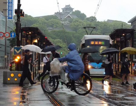 雨が降る中、通勤、通学を急ぐ人たち。後方は熊本城＝２８日午前、熊本市中央区