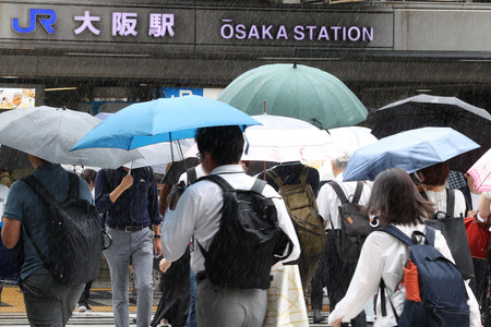 雨の中、傘を差してＪＲ大阪駅前を歩く人たち＝２１日午前、大阪市北区