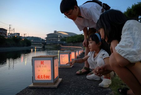 浦上川周辺で行われた「万灯流し」で、川辺に置かれた灯籠を見つめる子どもたち＝９日午後、長崎市