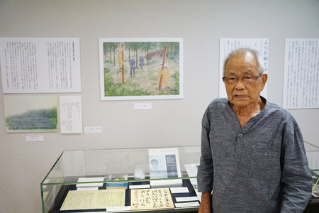 自身の証言を基にしたイラストの前に立つ石井利水さん＝７月３０日、福島県いわき市