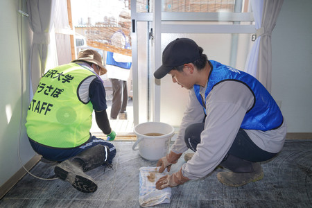 床上浸水した仮設住宅を掃除するボランティアの山田和輝さん（右）＝２５日午後、石川県輪島市