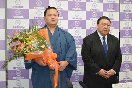 引退会見で花束を手に写真撮影に応じる元関脇妙義龍（左）。右は師匠の境川親方＝２６日、東京・両国国技館