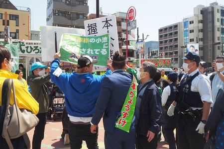 候補者の前で、プラカードを掲げる「つばさの党」の根本良輔氏（中央）ら＝４月２５日、東京都江東区