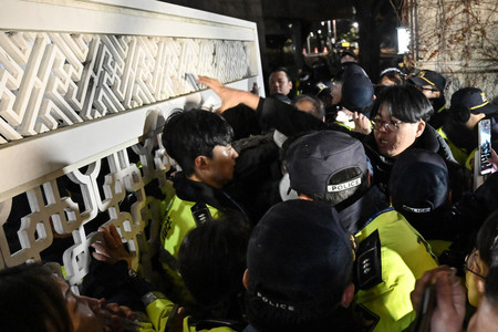 ３日夜、ソウルにある韓国国会の正門で人々と押し合う警官（ＡＦＰ時事）