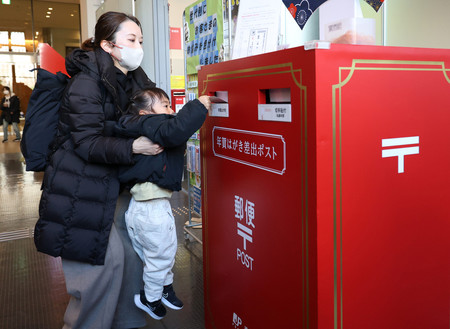 年賀状の受け付けが始まり、東京中央郵便局に置かれた特設ポストに投函（とうかん）する親子＝１５日午前、東京都千代田区