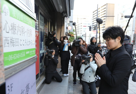 現場の雑居ビルの前で手を合わせる、亡くなったクリニック院長西沢弘太郎さんの妹伸子さん（右）＝１７日午前、大阪市北区