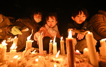 阪神大震災の追悼の集いで、ろうそくに火をともす親子＝１６日午後、兵庫県伊丹市の昆陽池公園