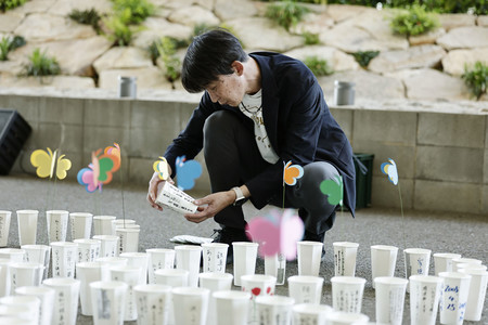 JR福知山線脱線事故の追悼行事を前に、ろうそくの入った紙コップを並べる犠牲者遺族の上田誠さん=24日午後、兵庫県尼崎市(代表撮影)