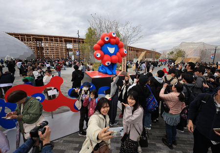 大阪・関西万博の公式キャラクター「ミャクミャク」像の前で写真を撮る人たち=13日、大阪市此花区