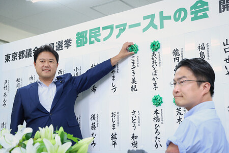 当選確実の候補者名に花を付ける地域政党「都民ファーストの会」の森村隆行代表(左)。右は乙武洋匡顧問=22日午後、東京都青梅市