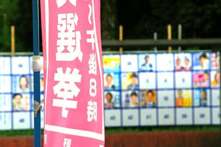 参院選の投票日を知らせる旗(手前)とポスター掲示板=17日、東京都日野市