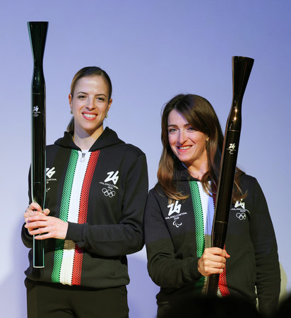 大阪・関西万博のイタリア館で初披露されたミラノ・コルティナ冬季五輪・パラリンピックの聖火リレートーチ。左は元フィギュアスケート選手のコストナーさん、右はパラ陸上のカイロニさん=14日午後、大阪市此花区