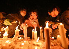 阪神大震災の追悼の集いで、ろうそくに火をともす親子＝１６日午後、兵庫県伊丹市の昆陽池公園