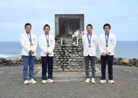 パリ五輪で獲得した銅メダルを胸に、硫黄島の故西竹一氏の石碑の前で写真に納まる「初老ジャパン」の４人（日本馬術連盟提供）