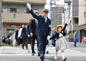 手を挙げて横断歩道を渡る筒井洋樹警視総監（手前左）と新１年生＝６日午後、東京都大田区