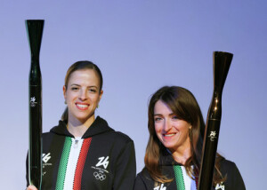 大阪・関西万博のイタリア館で初披露されたミラノ・コルティナ冬季五輪・パラリンピックの聖火リレートーチ。左は元フィギュアスケート選手のコストナーさん、右はパラ陸上のカイロニさん＝１４日午後、大阪市此花区